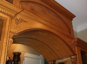 This arched wall bridge is atop a sink vanity which is carved from solid stone. The arched raised panel reflects the shape of the arched bottom and is further enhanced with acanthus corbels and dental molding on the sub crown molding.