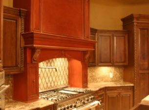 This amazing kitchen features a blend of painted and stained cabinetry. The custom range hood features a red base color with a dark Van Dyke Glaze. The maple cabinetry has a dark pecan stain with glaze.
