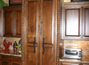 The butlers pantry is concealed by mounting cabinet doors to a 3'0" twin door and placing them between 2 pilasters with rope molding fluting. This creates the appearance of cabinetry rather than an interior door.
