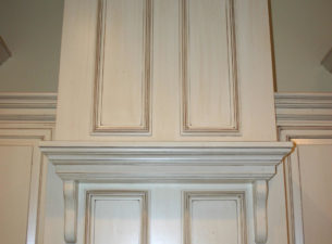 This custom range hood features onlaid astragal molding and a mantle like shelf which is groved for plate display should the client so wish to display one.  White conversion varnish finish w/ distressing, sand through, and a VanDyke Glaze finish.