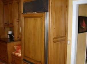 Refrigerator is shown with panelized front. The 2 end panels are 3" wide and faced with triple bead fluting. A wall bridge cabinet spans the top between the panels. The crown kit then wraps the top and steps out and around the panel flutes.